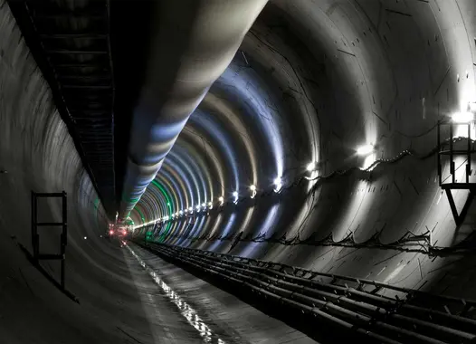 Interior view of a long, illuminated tunnel with reflective walls and ceiling, showing light fixtures and construction elements