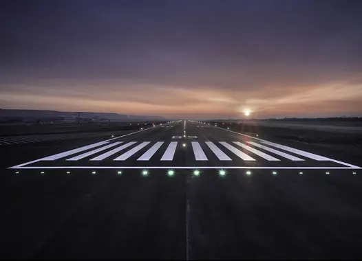 A runway at twilight with the sun near the horizon and green edge lights