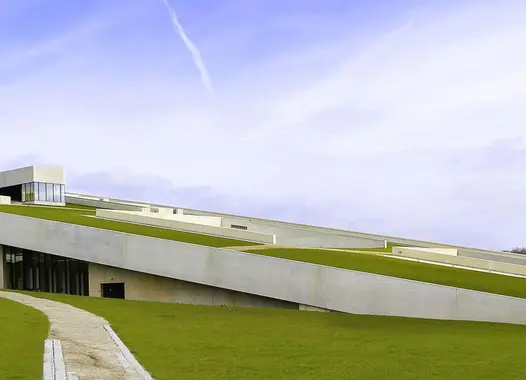 A modern building with an expansive, sloping green roof that blends seamlessly into the surrounding grassy landscape. The architecture is notable for its eco-friendly design, integrating the structure harmoniously with the natural environment.