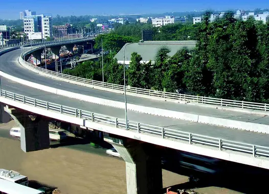 An elevated roadway curving to the left as it spans across the frame. Below the roadway, there are buildings and trees visible, indicating an urban or suburban setting.