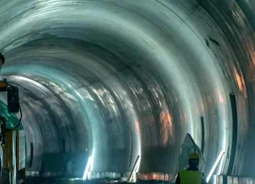 Curved tunnel with concentric rings and reflective surfaces, illuminated by lights along its length, creating an illusion of depth and continuity.